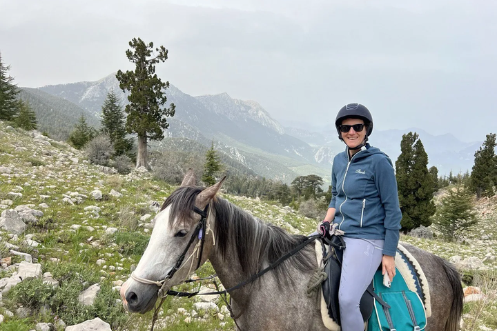 A rider wearing a helmet on a grey horse in a rocky mountain landscape; photograph from Erendiz’s Hilal Ranch image collection.