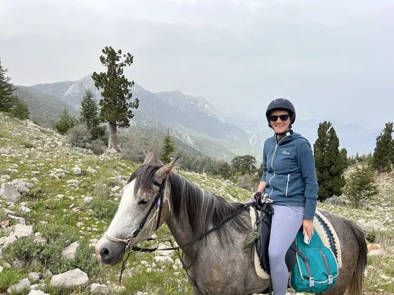 Una amazona con casco sobre un caballo gris en un paisaje montañoso rocoso; fotografía de la colección de Hilal Ranch de Erendiz.