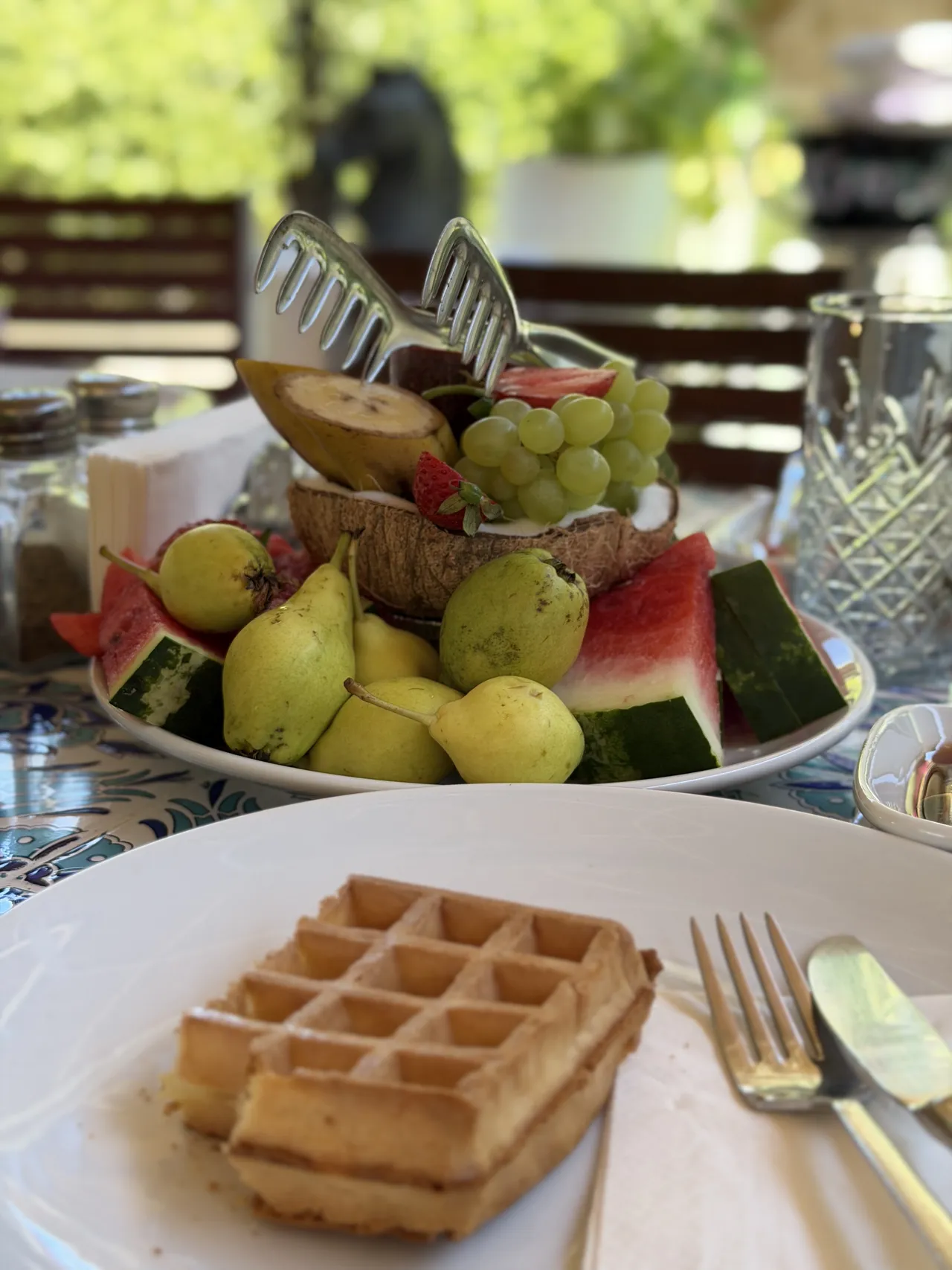 A waffle at a set table, with a platter of fresh fruit behind it.